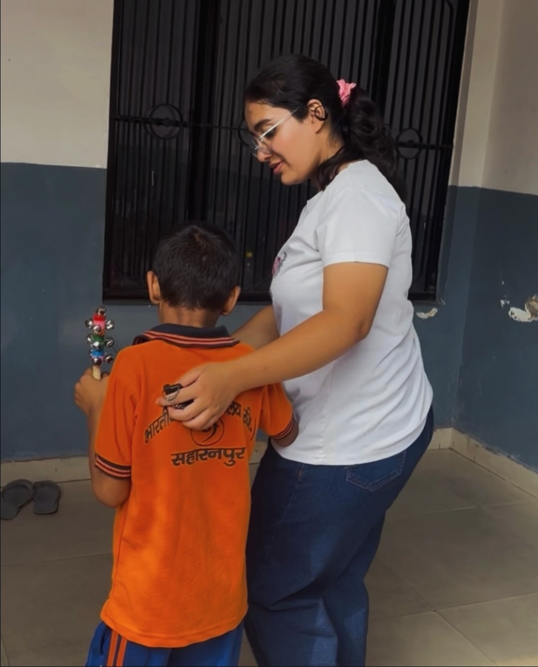 An Arunarya volunteer guiding a visually impaired boy holding a wooden bell rattle